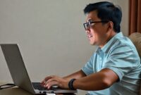 Ilustrasi seorang pengguna yang tersenyum sambil menonton film di laptop dengan VLC Media Player Portable terbuka di layar. Laptop terhubung ke flash drive.