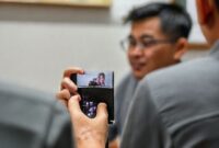 Seorang pria sedang menonton video di iPhone yang disangga oleh Hikawa Phone Grip & Stand di atas meja.