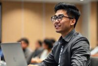 Seorang profesional muda sedang bersemangat mengikuti pelatihan digital, dengan laptop dan catatan di depannya, menunjukkan fokus dan antusiasme.