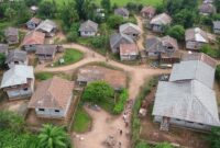 Aerial view of a resilient Sumatran village being rebuilt after a disaster, showing new earthquake-resistant homes, green spaces, and community facilities, with active construction and community members working together.