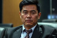 Seorang karyawan kantor yang sedang duduk sendirian di mejanya pada larut malam, dengan ekspresi wajah yang ketakutan. Latar belakang kantor yang gelap dan sepi.